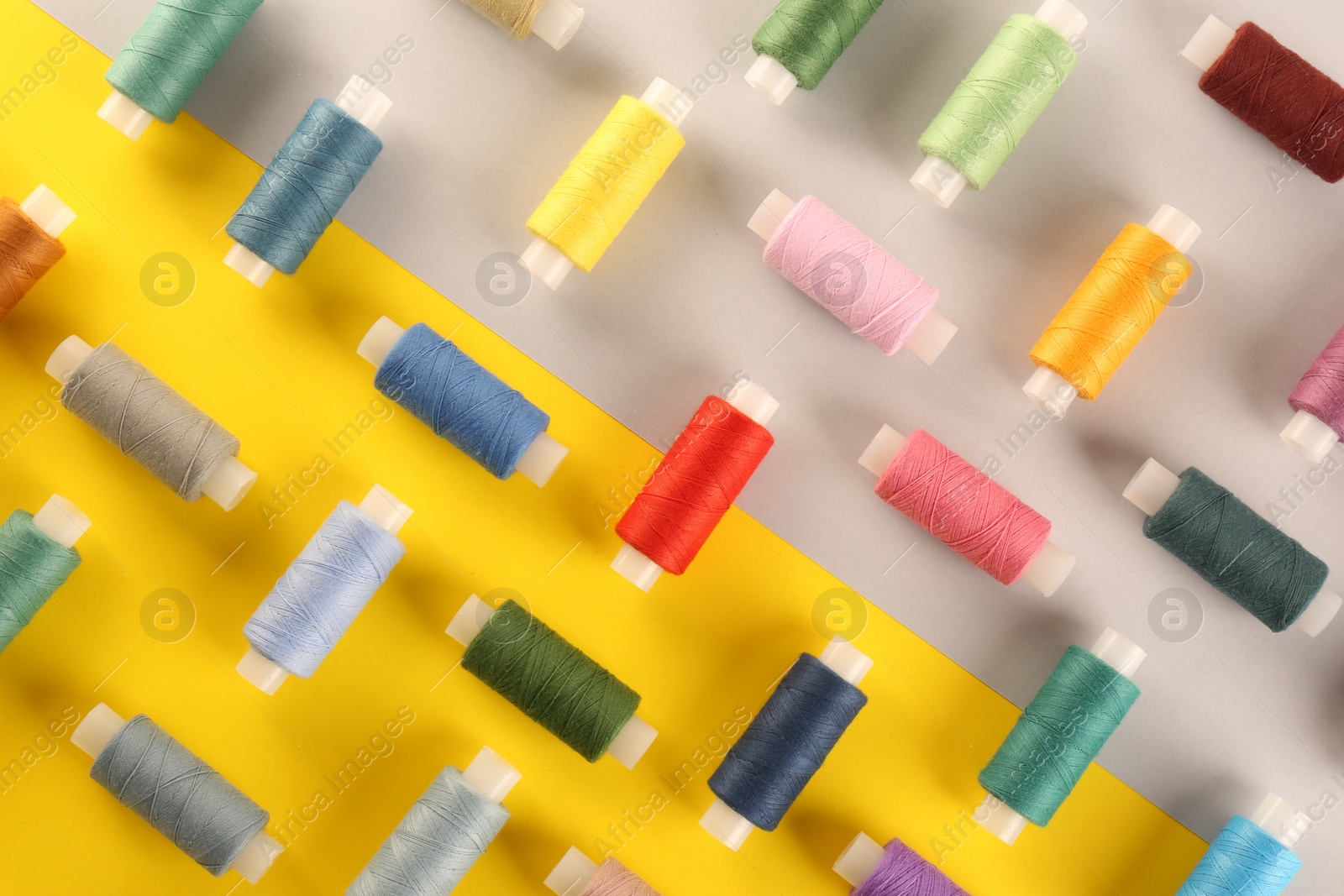 Photo of Different sewing threads on color background, flat lay