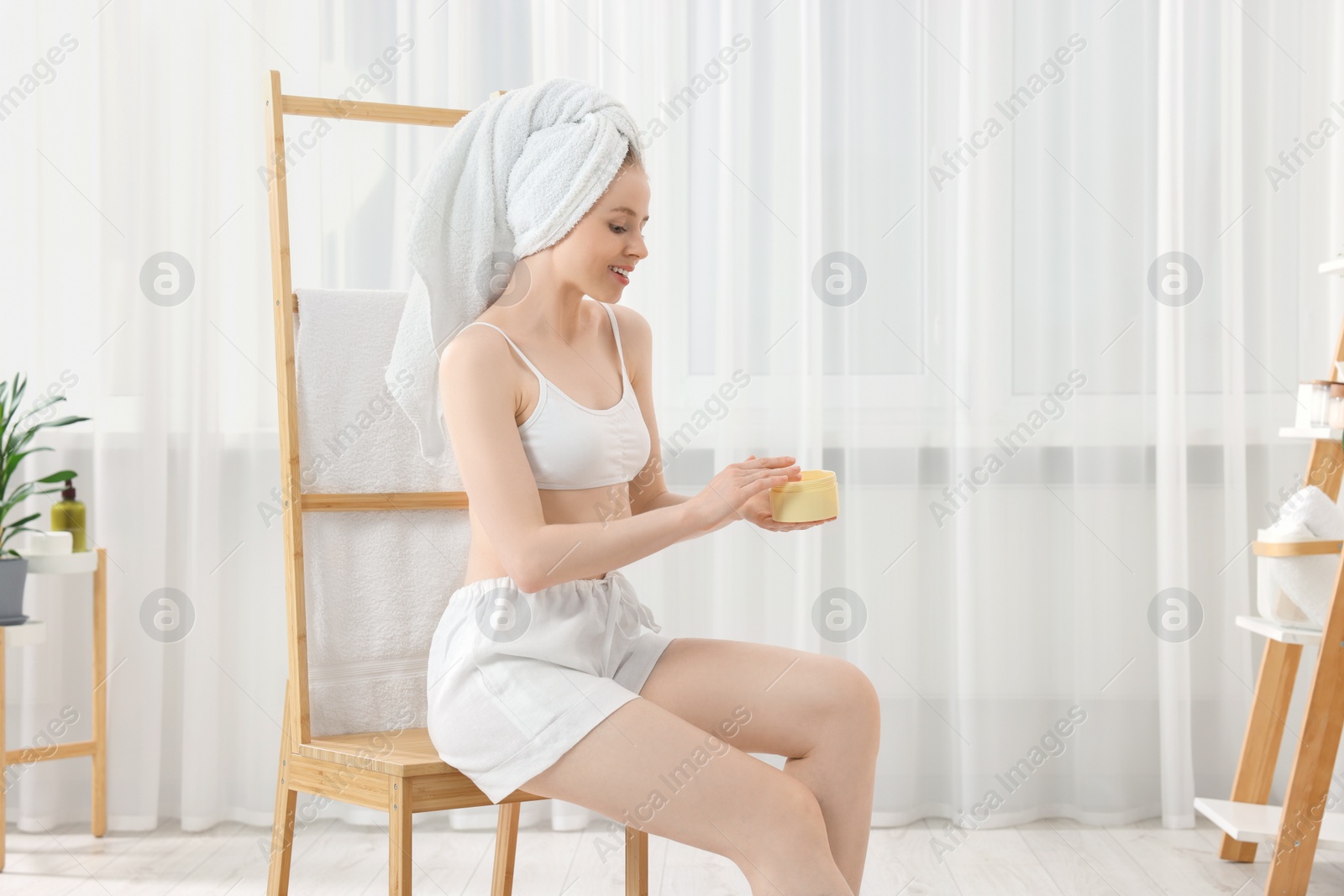 Photo of Beautiful young woman with jar of body cream indoors