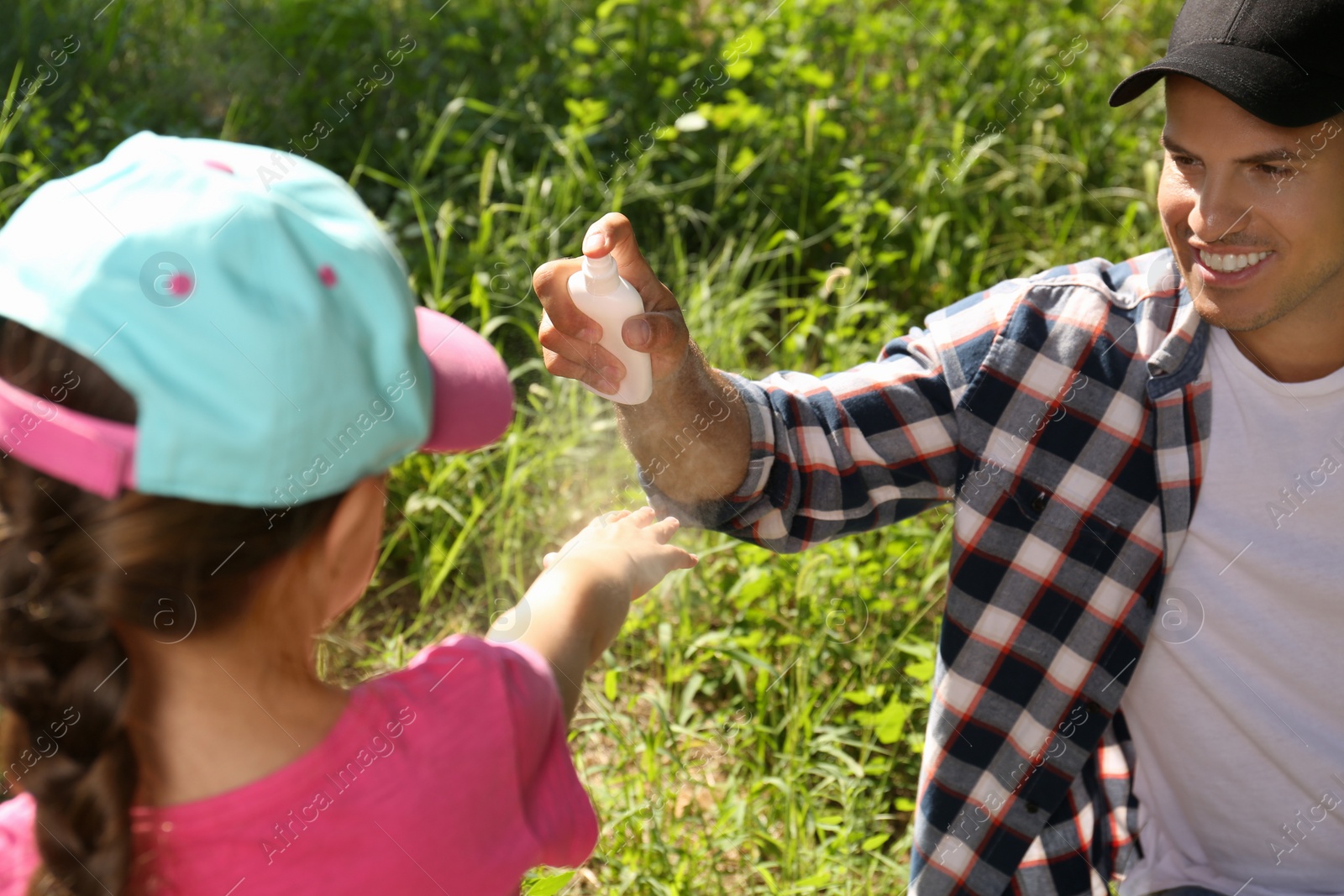 Photo of Father spraying tick repellent on his little daughter's arm during hike in nature