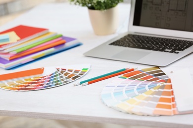 Photo of Paint color palette samples and laptop on table, closeup