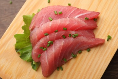 Photo of Tasty sashimi (pieces of fresh raw tuna with green onion) on wooden board, above view