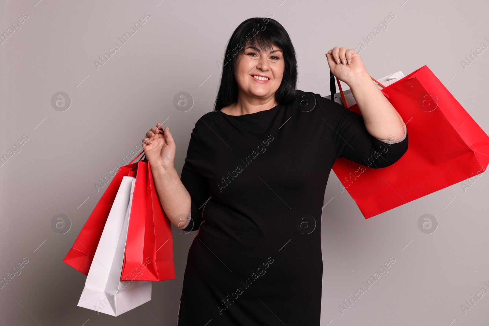 Photo of Beautiful overweight mature woman with shopping bags on light grey background