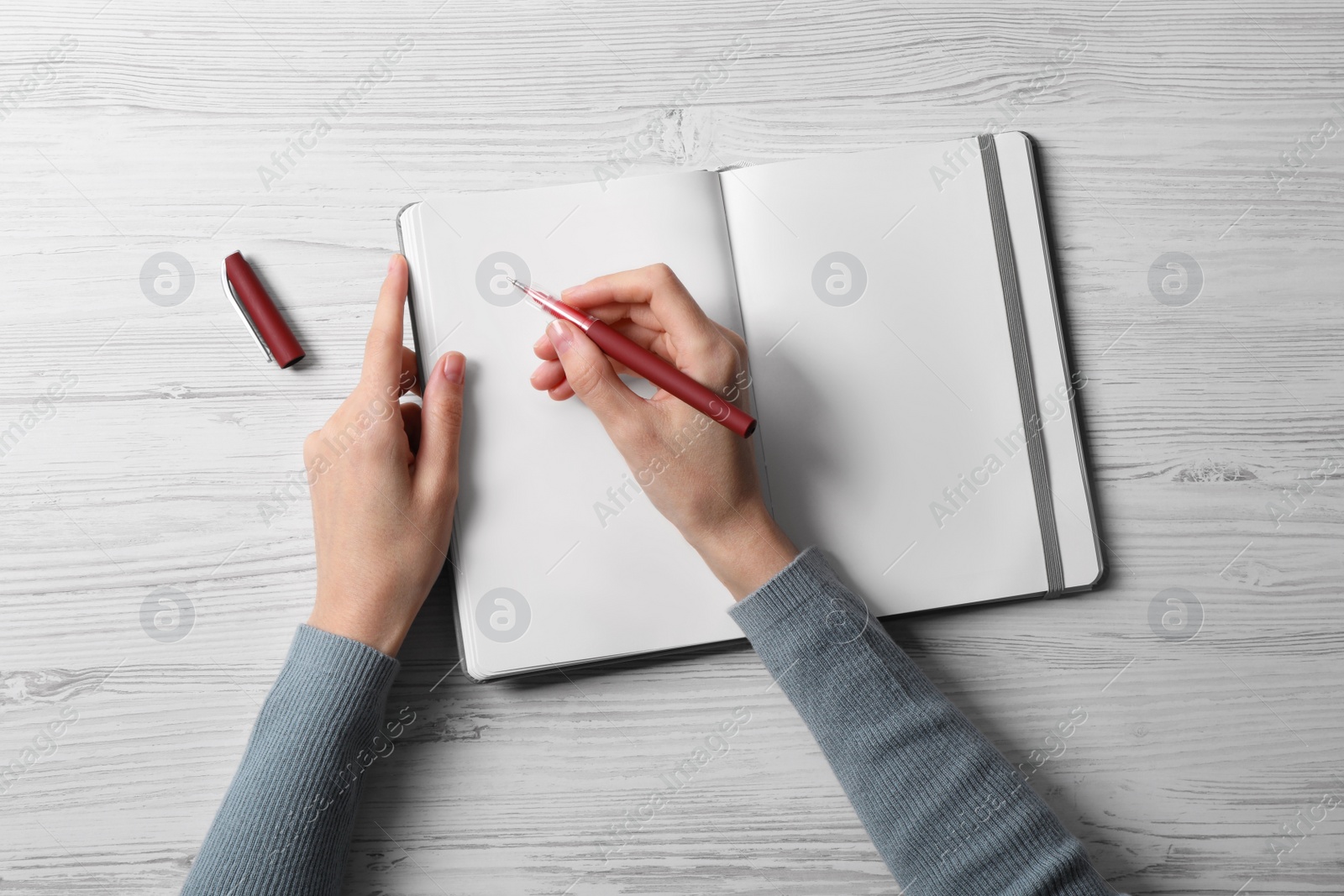 Photo of Woman writing in notebook at white wooden table, top view