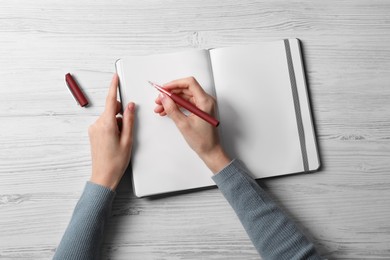 Photo of Woman writing in notebook at white wooden table, top view