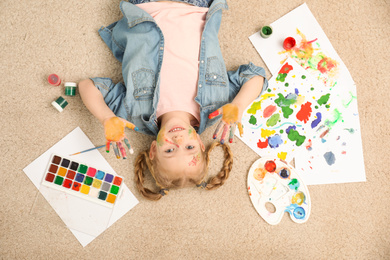 Photo of Cute little child with painted face and palms on floor, top view