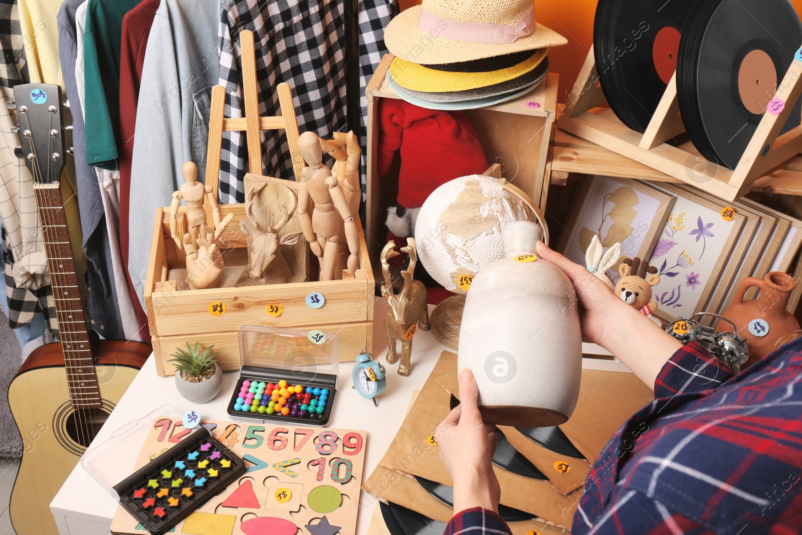 Photo of Woman holding vase near table with many different stuff indoors, closeup. Garage sale