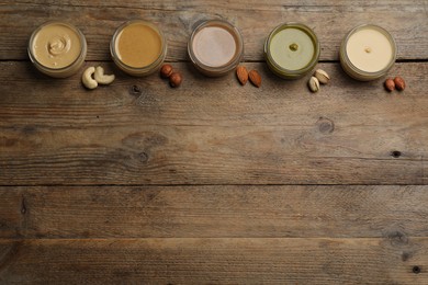 Jars with butters made of different nuts and ingredients on wooden table, flat lay. Space for text
