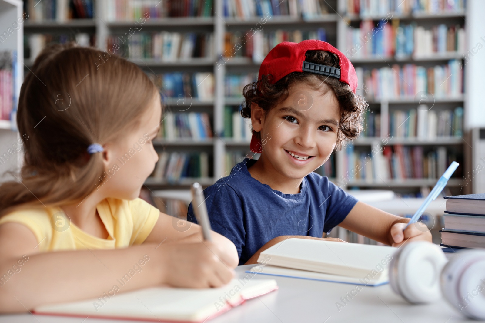 Photo of Little children writing at table with books in library reading room