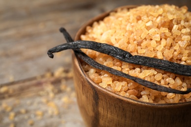 Photo of Bowl of aromatic vanilla sugar and sticks on wooden background, closeup