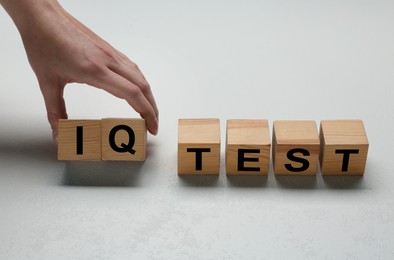 Photo of Woman taking cubes with text IQ Test on light background, closeup