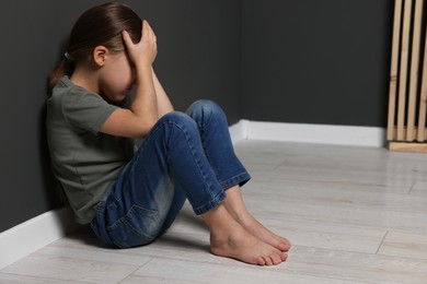 Photo of Child abuse. Upset girl sitting on floor near grey wall, space for text