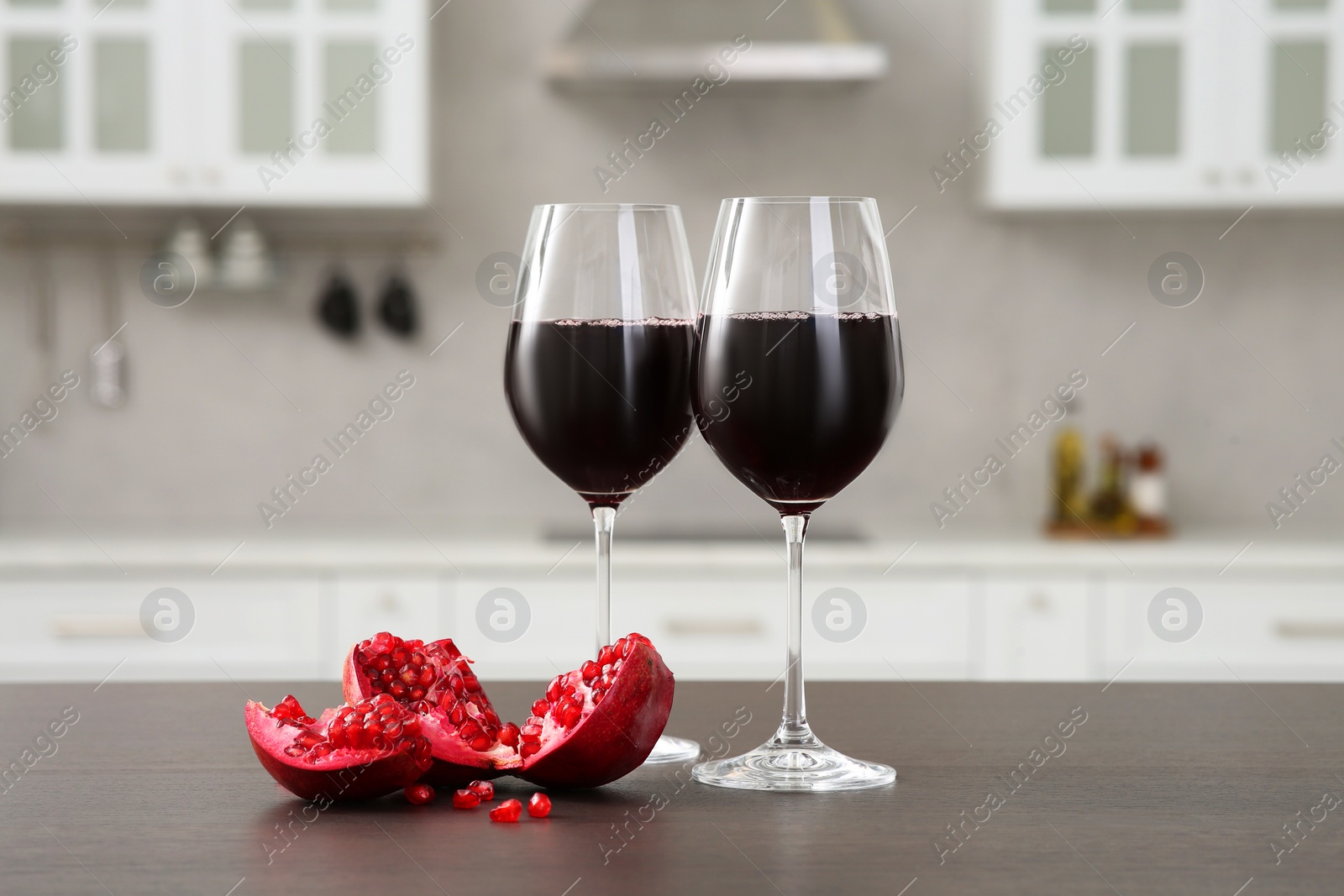 Photo of Glasses of red wine and fresh pomegranate on countertop in kitchen