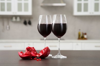 Photo of Glasses of red wine and fresh pomegranate on countertop in kitchen