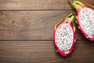 Photo of Halves of delicious dragon fruit (pitahaya) on wooden table, flat lay. Space for text
