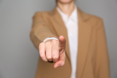 Photo of Businesswoman pointing at something on grey background, closeup. Finger gesture