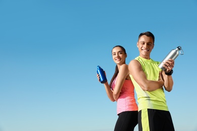 Photo of Young sporty couple with water bottles against blue sky on sunny day. Space for text