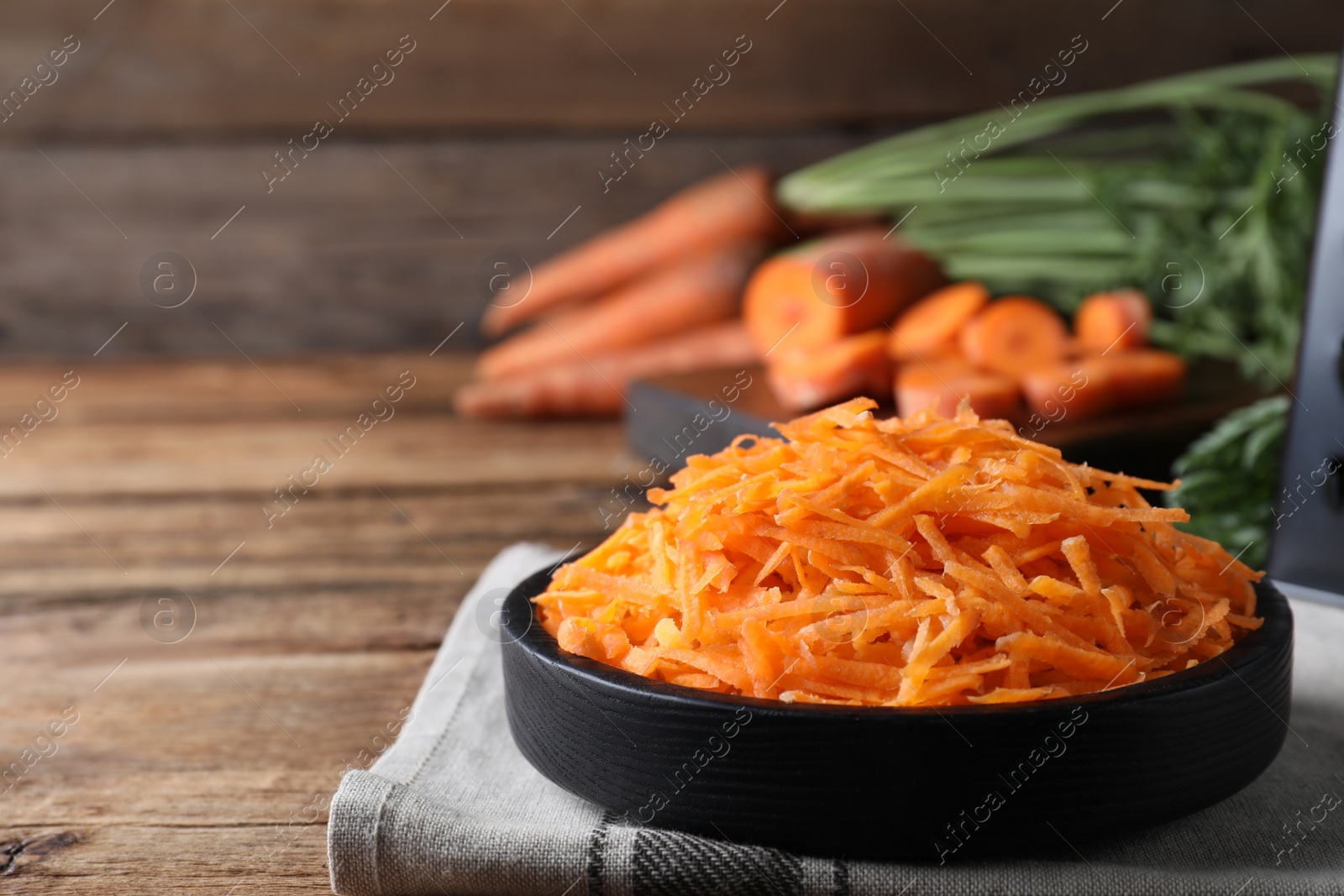 Photo of Grated carrot in plate on wooden table. Space for text