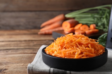 Photo of Grated carrot in plate on wooden table. Space for text