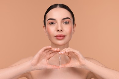 Photo of Beautiful young woman holding skincare ampoule on beige background