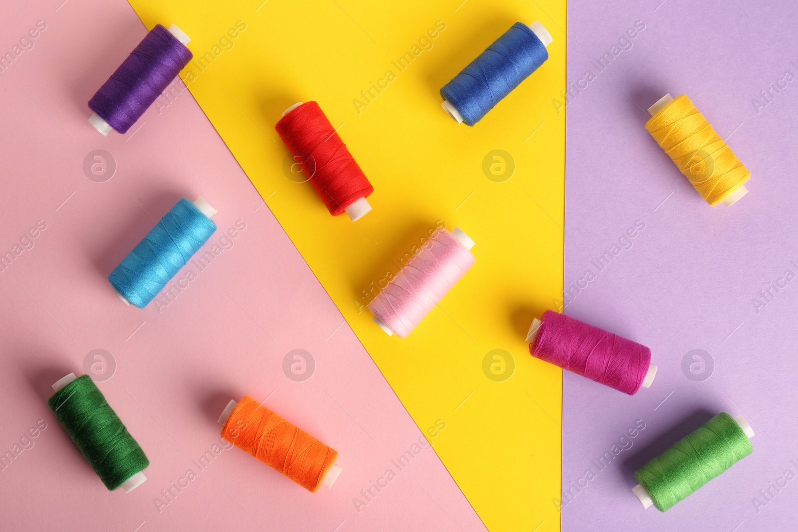 Photo of Different sewing threads on color background, flat lay