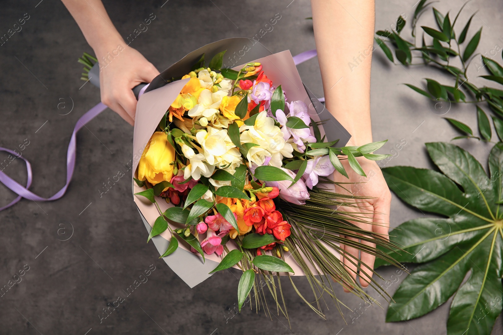 Photo of Woman with beautiful bouquet of freesia flowers on grey background