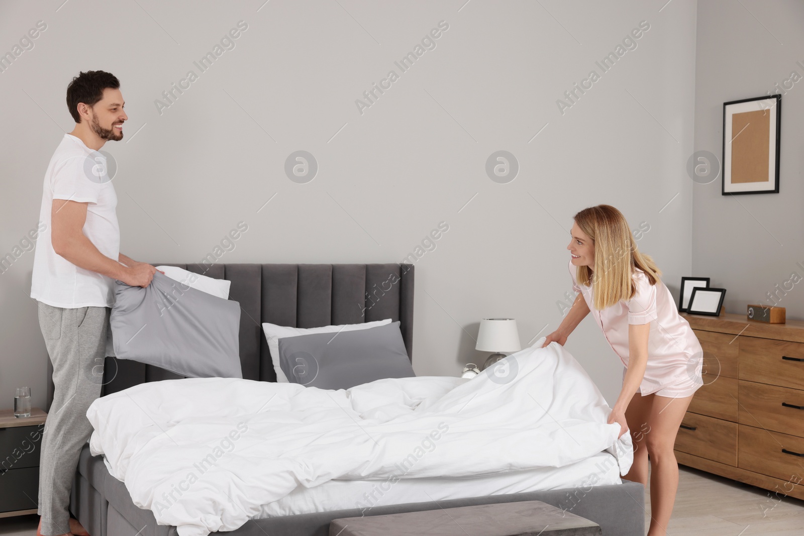 Photo of Couple changing bed linens in room. Domestic chores