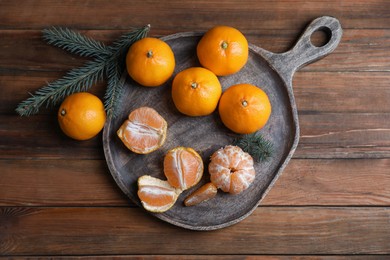Tray with delicious ripe tangerines and fir branches on wooden table, flat lay