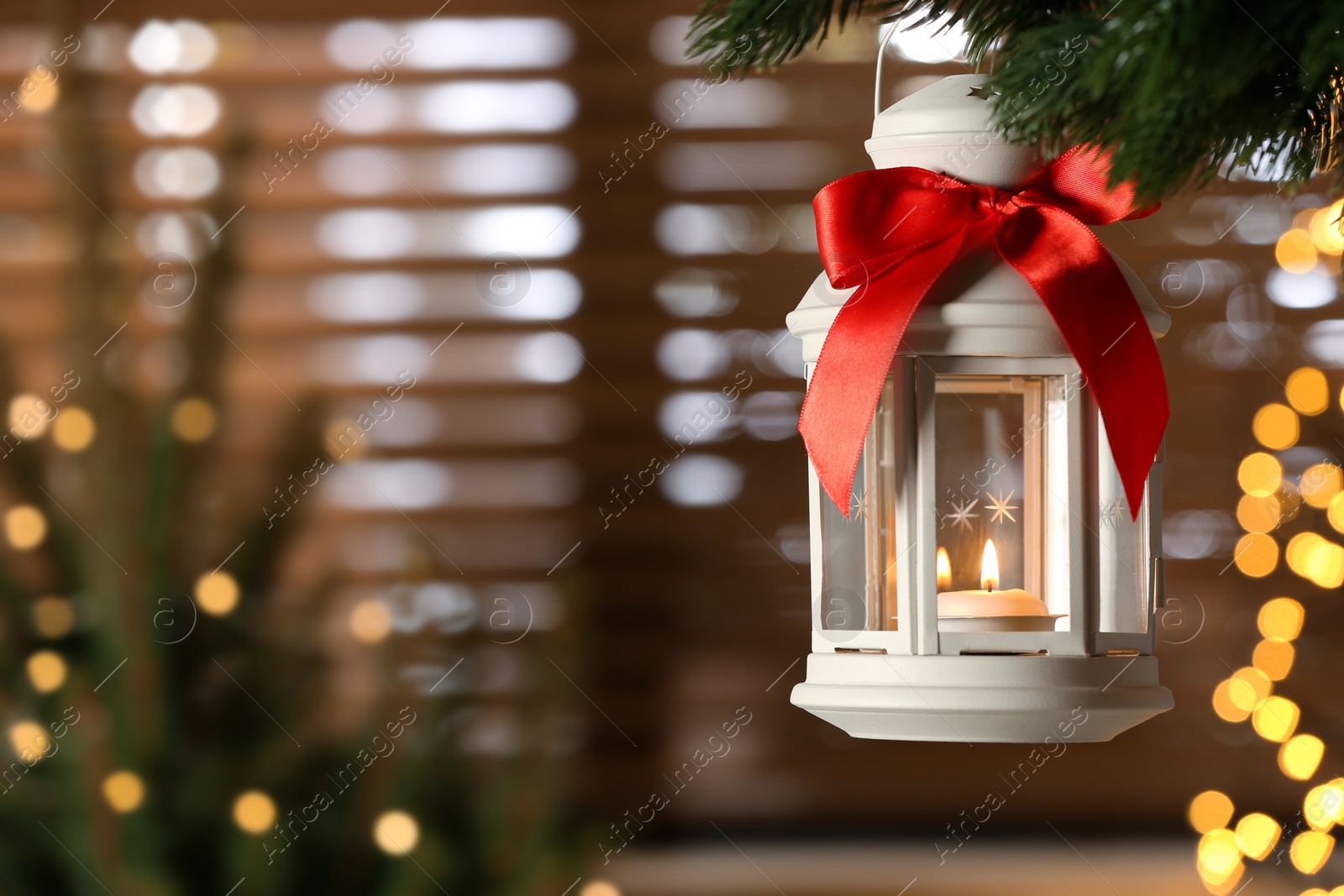 Photo of Beautiful Christmas lantern with burning candle hanging on fir tree branch in room. Space for text