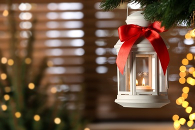 Photo of Beautiful Christmas lantern with burning candle hanging on fir tree branch in room. Space for text