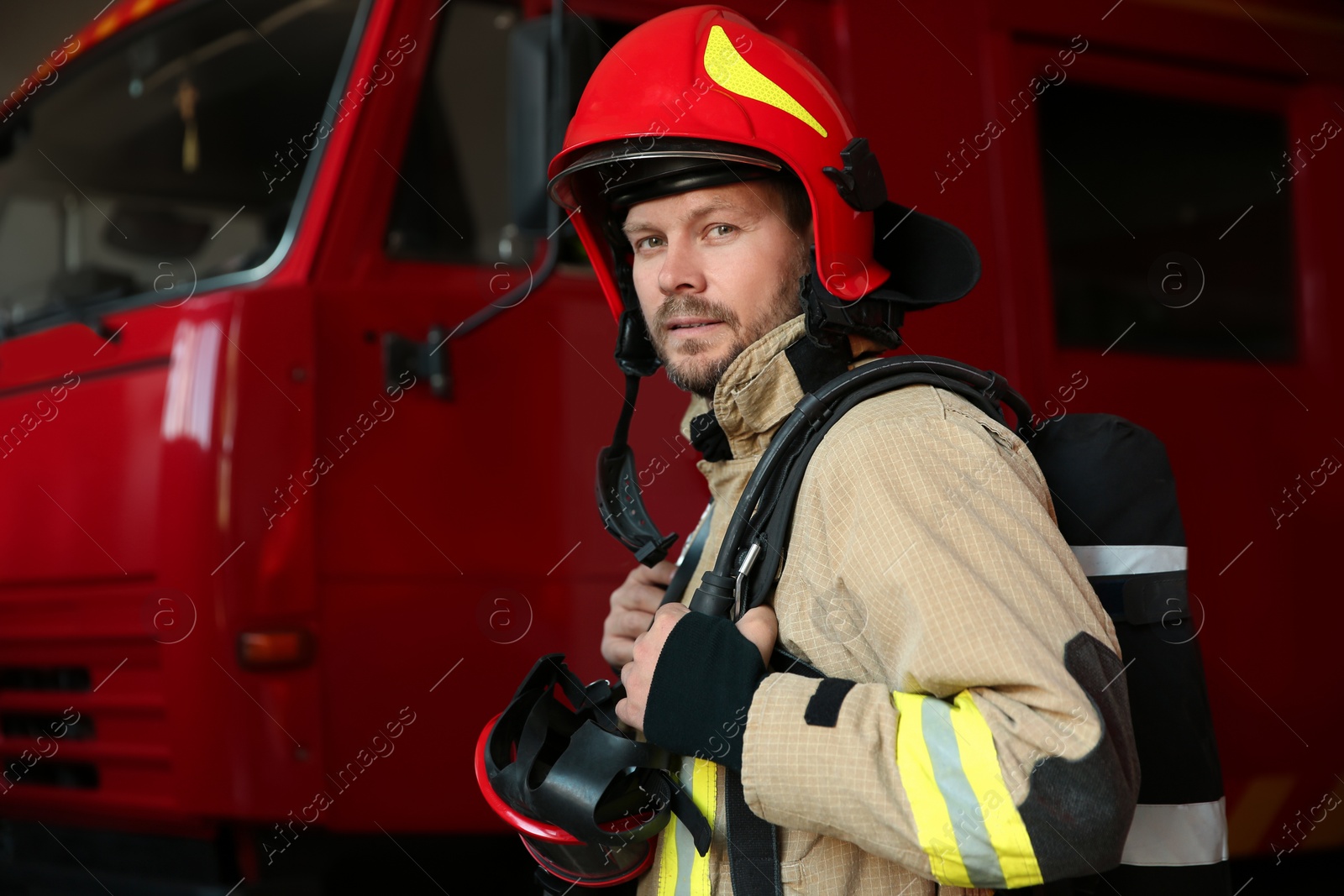 Photo of Portrait of firefighter in uniform near red fire truck at station