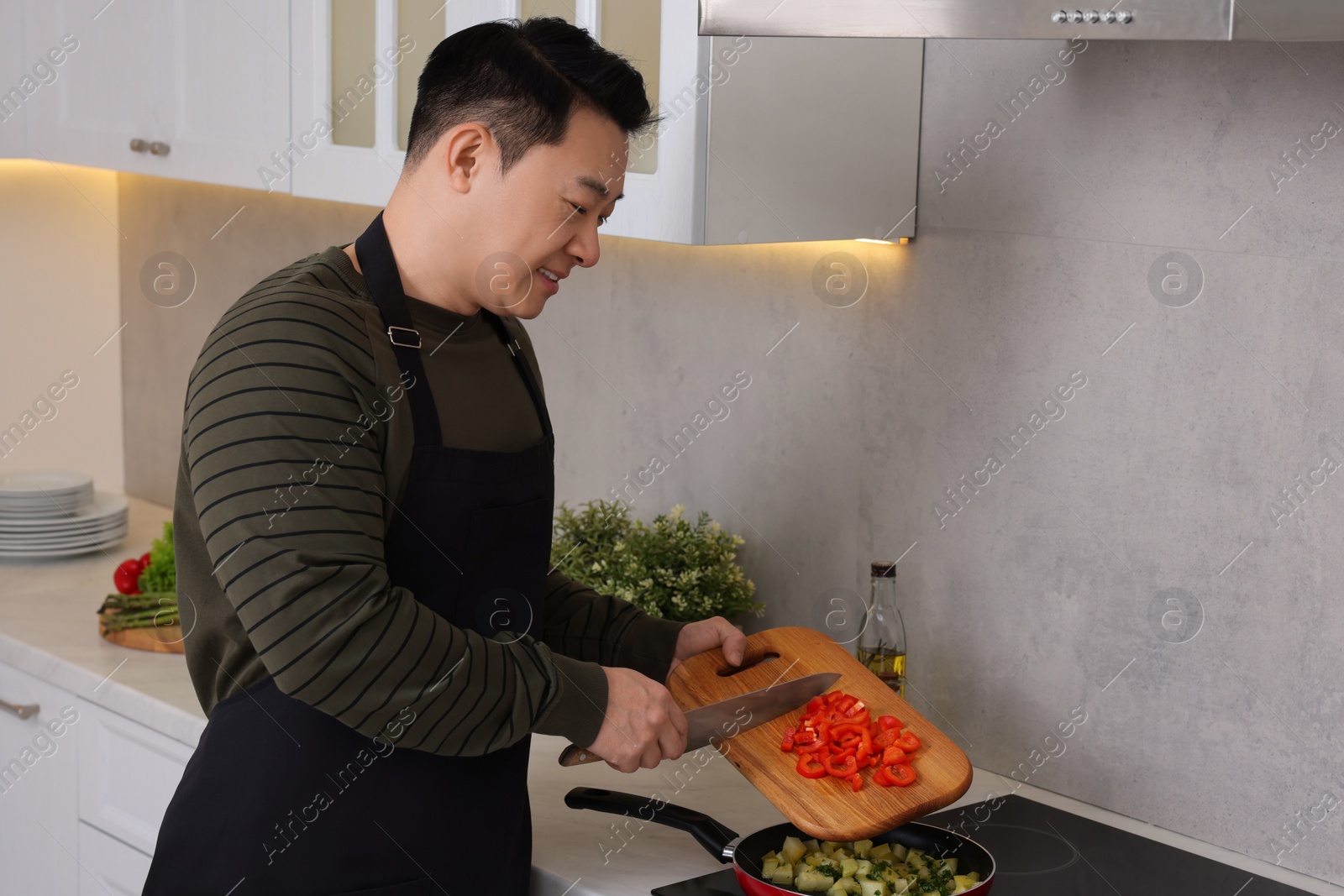 Photo of Cooking process. Man adding cut bell pepper into frying pan in kitchen, space for text