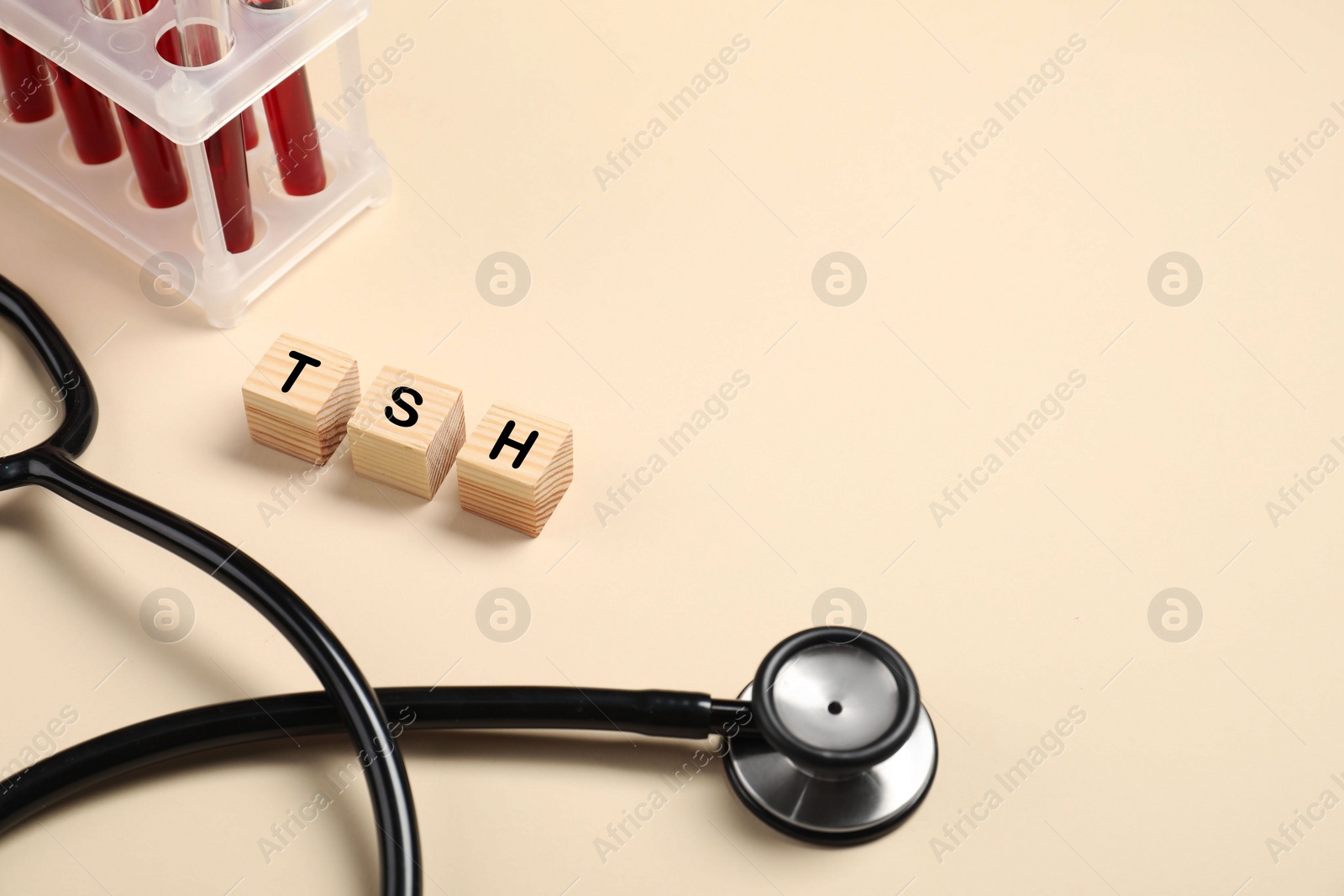 Photo of Endocrinology. Stethoscope, wooden cubes with thyroid hormones and blood samples in test tubes on beige background. Space for text