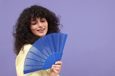 Photo of Happy woman holding hand fan on purple background. Space for text