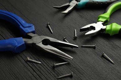 Photo of Different pliers and nails on black wooden table, closeup