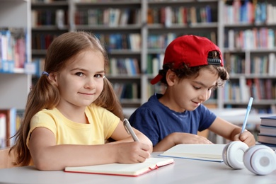Photo of Little children writing at table with books in library reading room