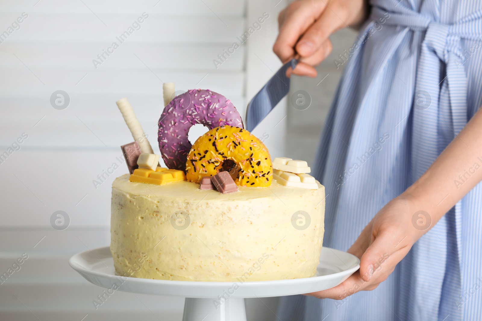 Photo of Woman cutting delicious cake decorated with sweets indoors, closeup