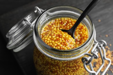 Photo of Whole grain mustard and spoon in jar on table, closeup