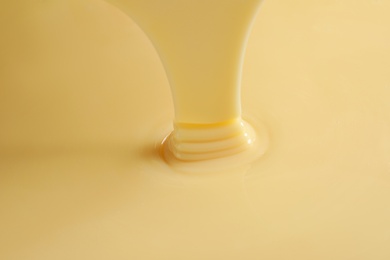 Photo of Tasty pouring condensed milk as background, closeup. Dairy product