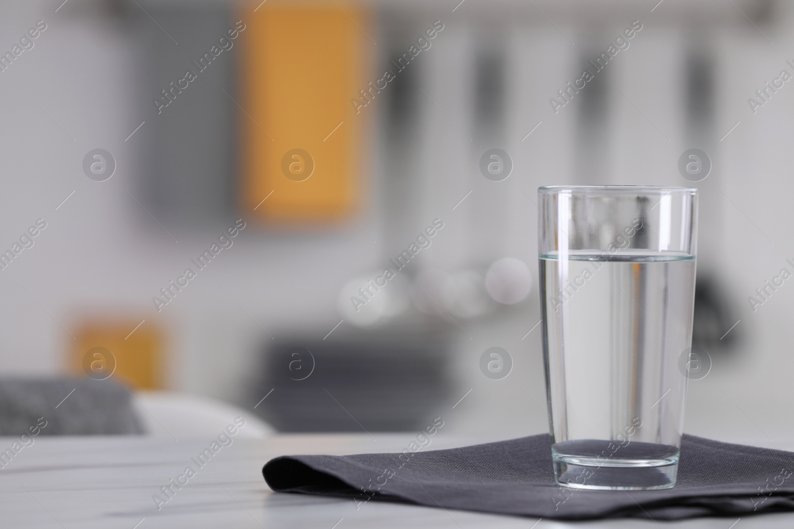 Photo of Glass of water and napkin on white table against blurred background. Space for text