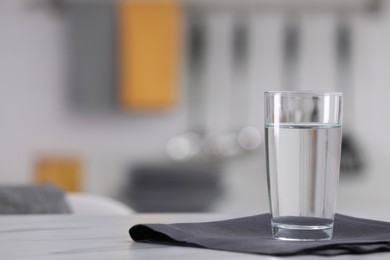 Photo of Glass of water and napkin on white table against blurred background. Space for text