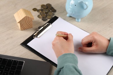 Photo of Woman planning budget, closeup. House model, coins and piggy bank on wooden table