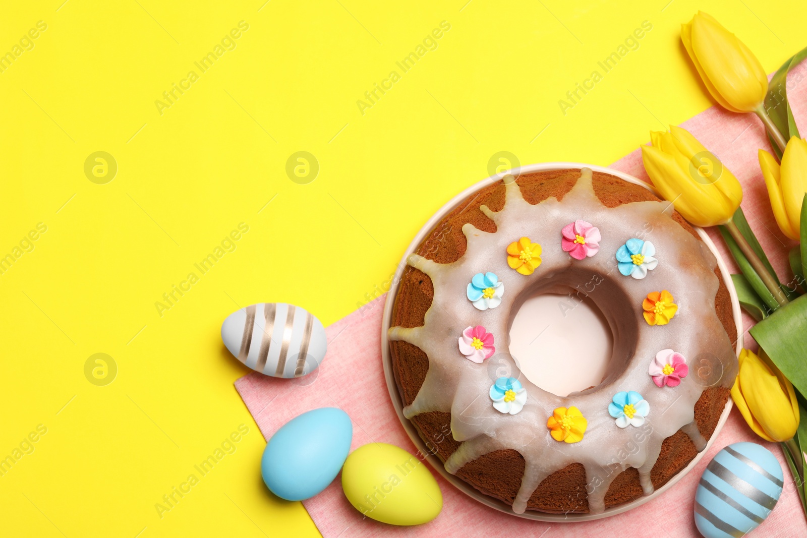 Photo of Delicious Easter cake decorated with sprinkles near beautiful tulips and painted eggs on yellow background, flat lay. Space for text