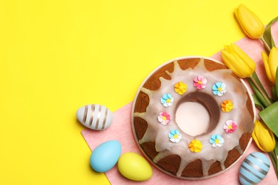 Photo of Delicious Easter cake decorated with sprinkles near beautiful tulips and painted eggs on yellow background, flat lay. Space for text