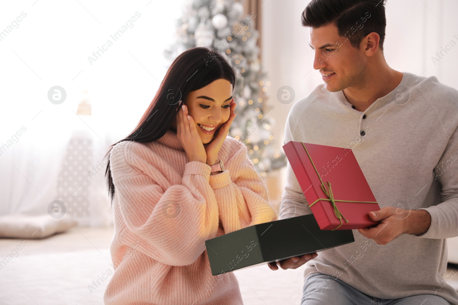 Photo of Couple opening gift box in room with Christmas tree