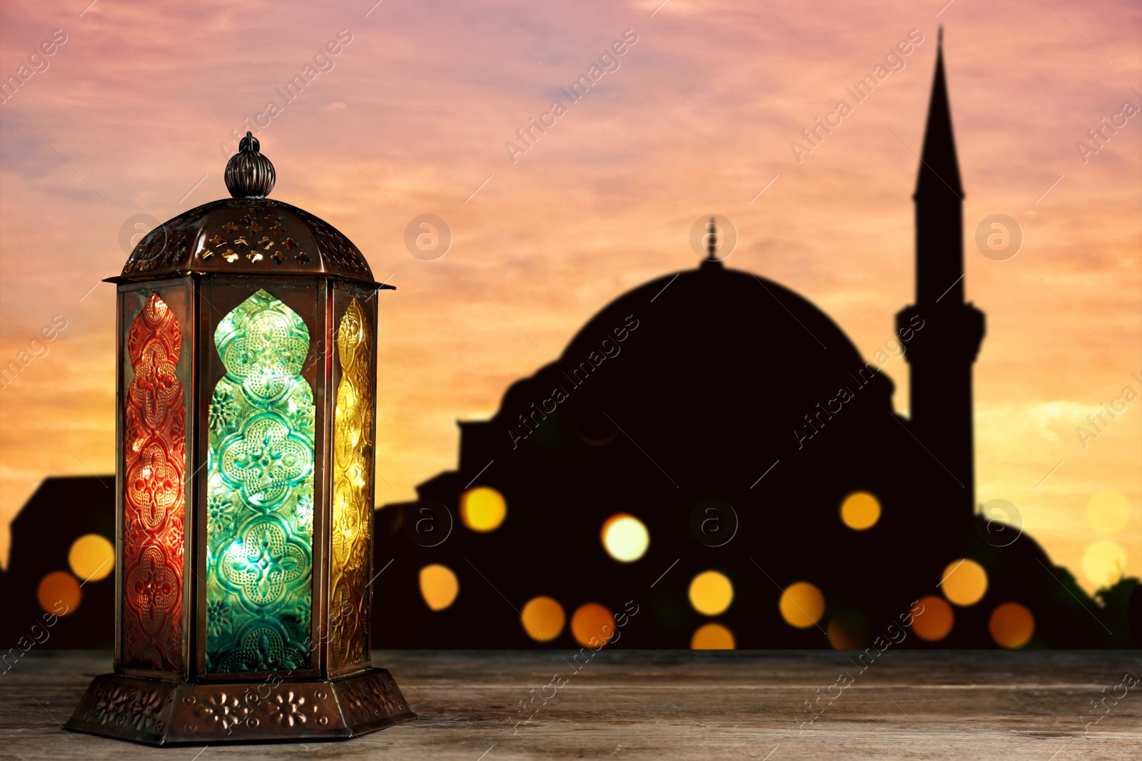 Image of Decorative Arabic lantern on wooden surface and silhouette of mosque at sunset on background, space for text