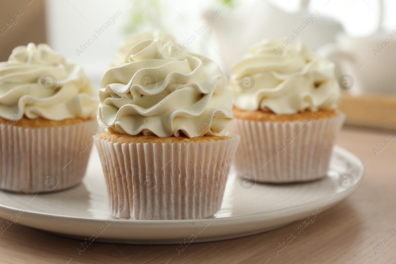 Photo of Tasty cupcakes with vanilla cream on light wooden table, closeup