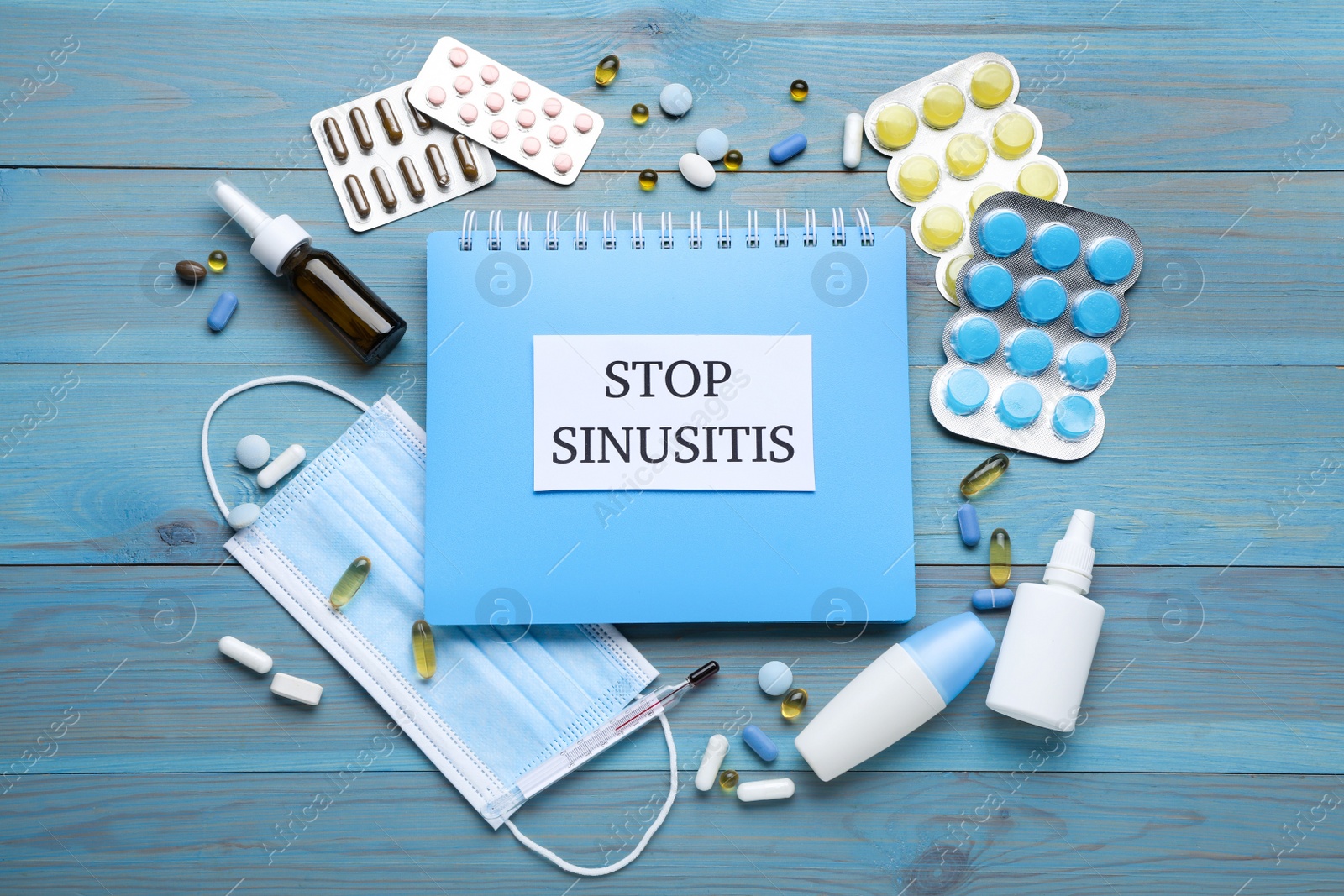 Photo of Notebook with word SINUSITIS, medical mask and different drugs on light blue wooden background, flat lay