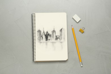 Sketch of cityscape in notebook, pencil and eraser on grey table, flat lay