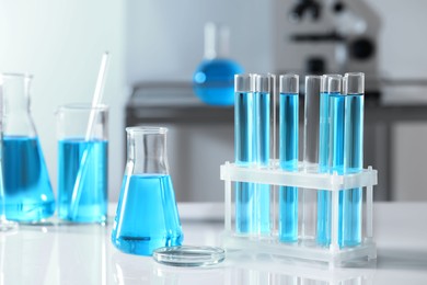 Photo of Test tubes with light blue liquid and different laboratory glassware on table
