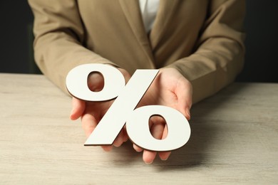 Photo of Woman holding percent sign at wooden table, closeup